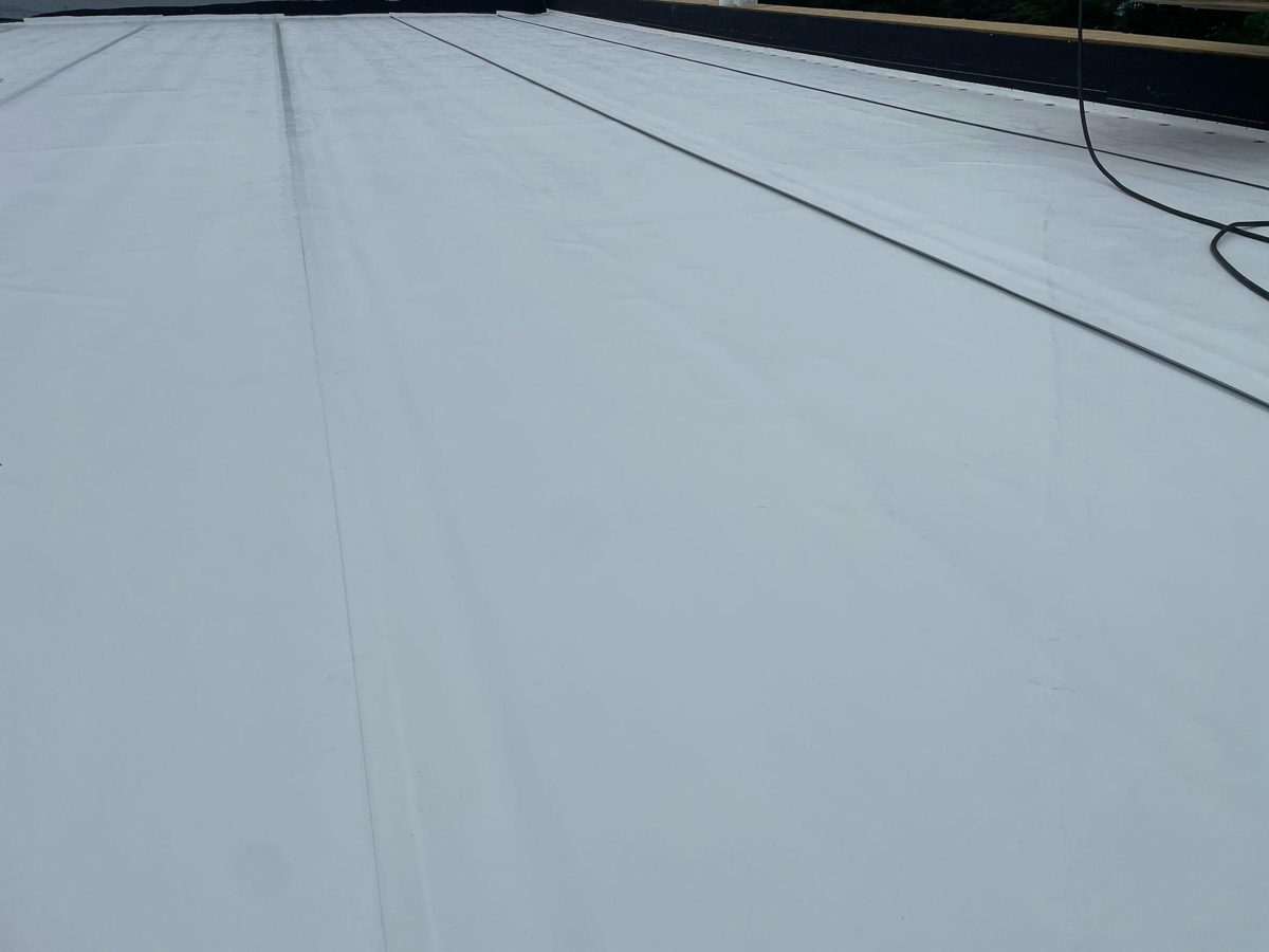 A finished white TPO roof with long welded seams running across it